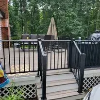 Black fenced deck with stairs, trees in the background. A small umbrella stands near the deck.