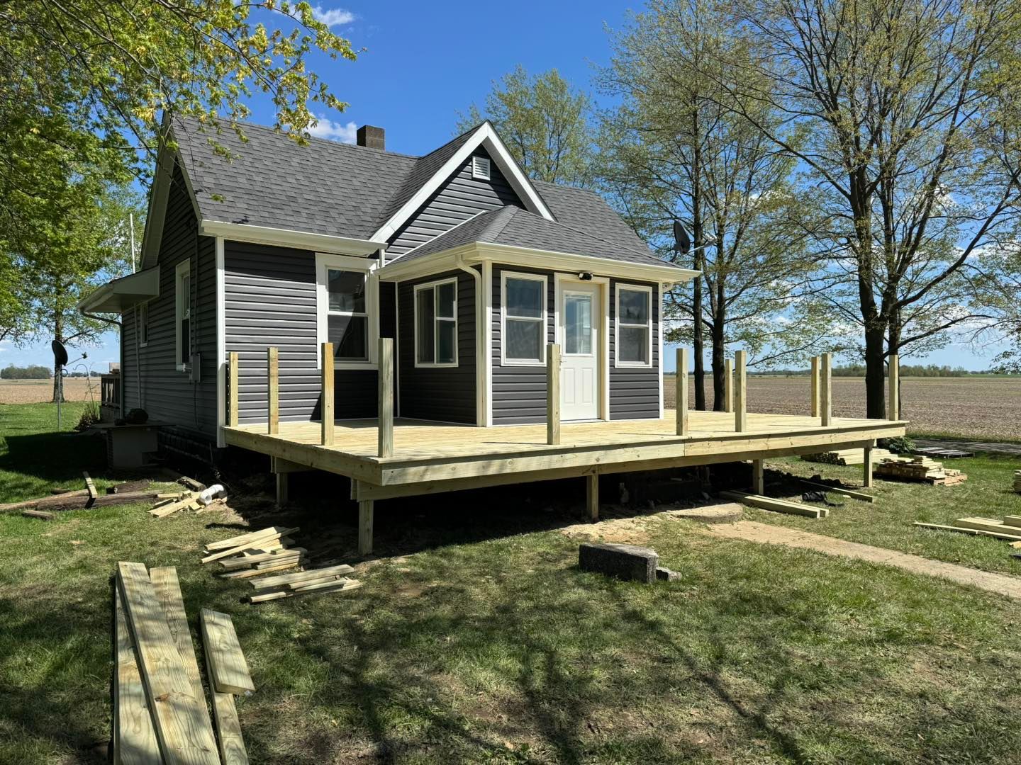 A gray house with a new wooden deck is under construction. Located in a grassy field.