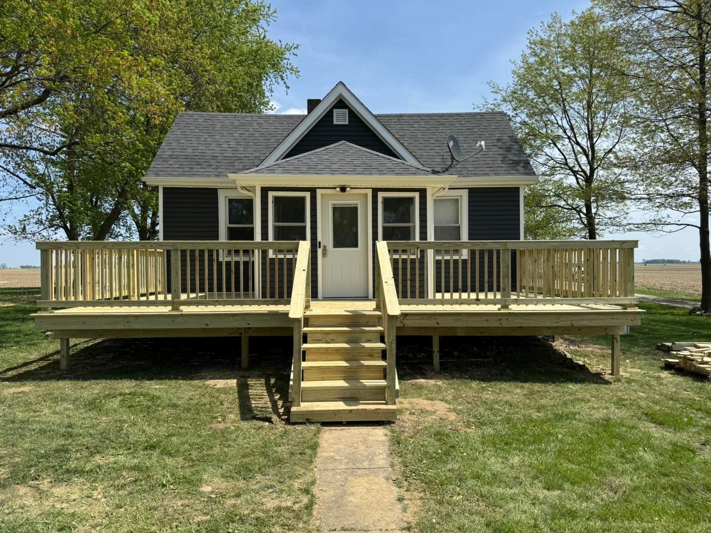 House with pergola under construction; new concrete patio, green grass, trees in background.