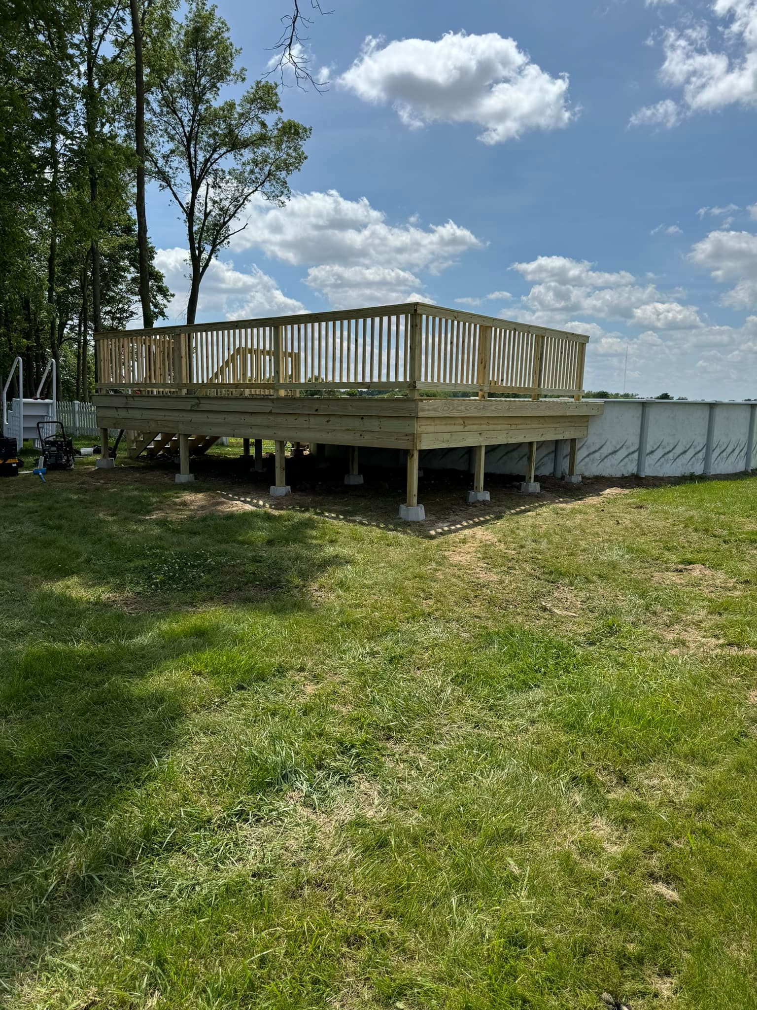 Wooden deck elevated on concrete blocks in a grassy yard under a blue sky.