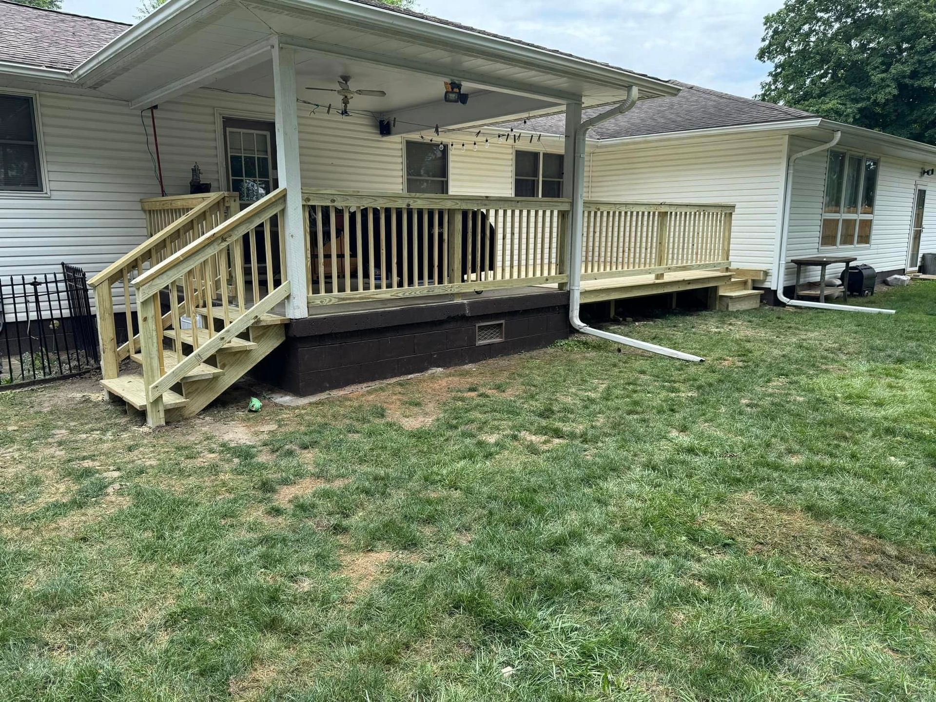 A newly built wooden deck attached to a white house with stairs and a railing, surrounded by green grass.