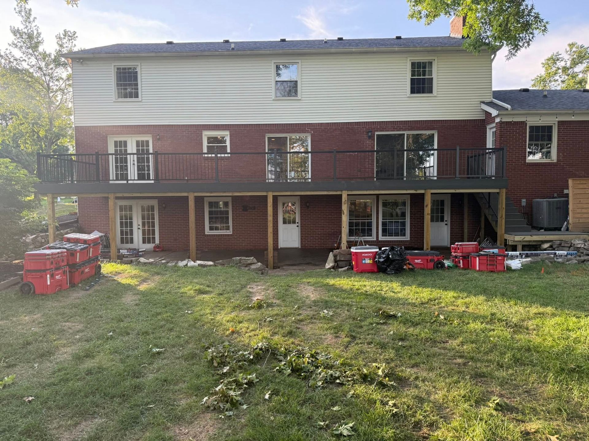 Back of two-story house with red brick and beige siding, a deck, and yard with construction equipment.