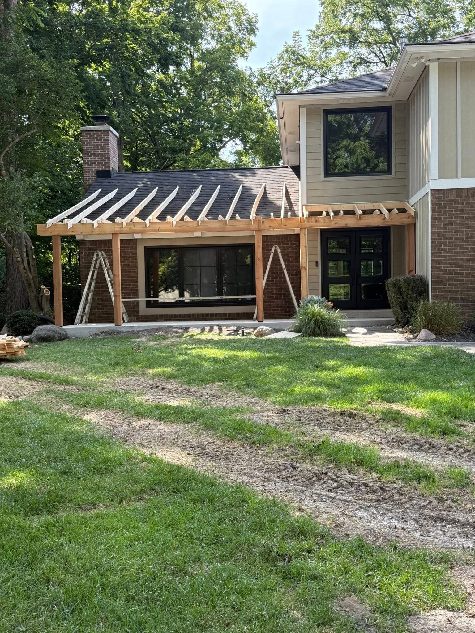 House exterior with pergola under construction; light brown siding, green lawn.