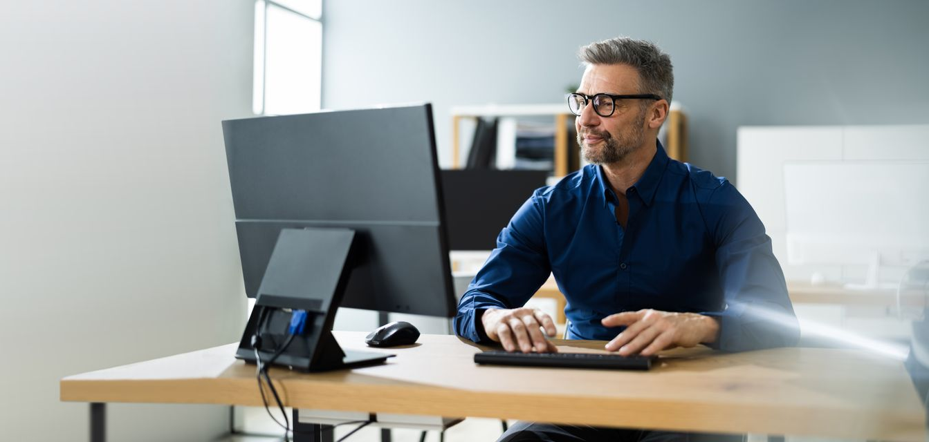 Man typing at desk with desktop computer in a bright office room