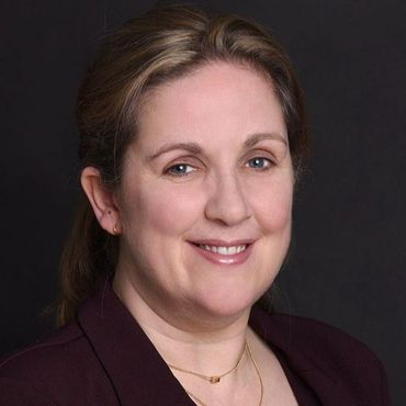 A woman wearing a purple jacket and a gold necklace is smiling for the camera.