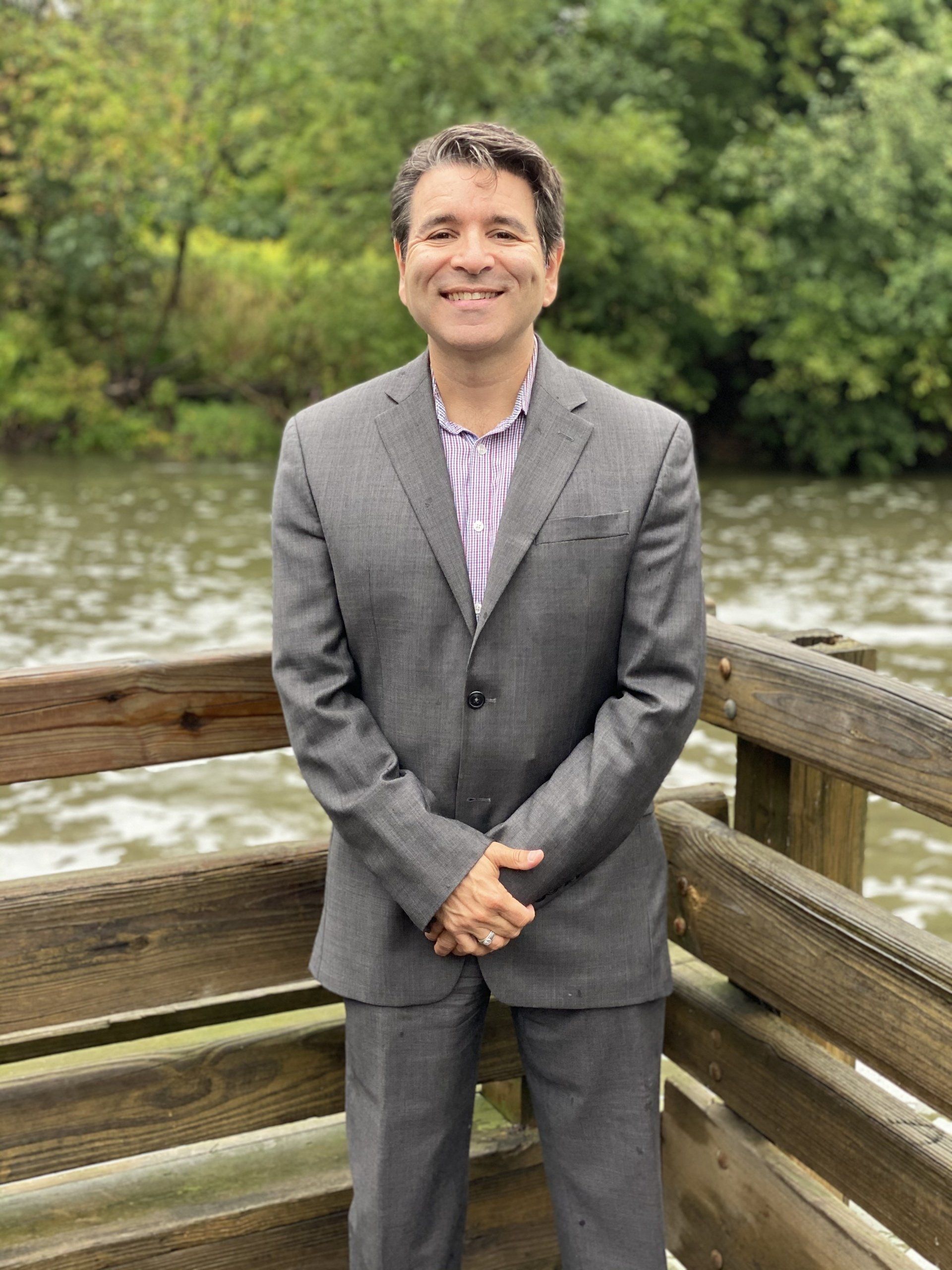 A man in a suit is standing on a wooden bridge overlooking a body of water.