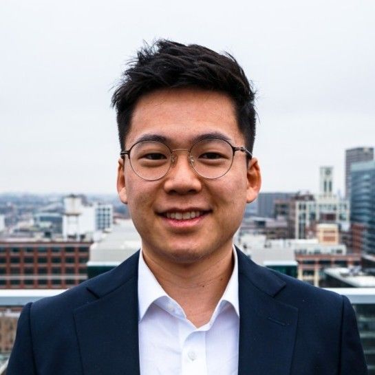 A young man wearing glasses and a suit is smiling for the camera.