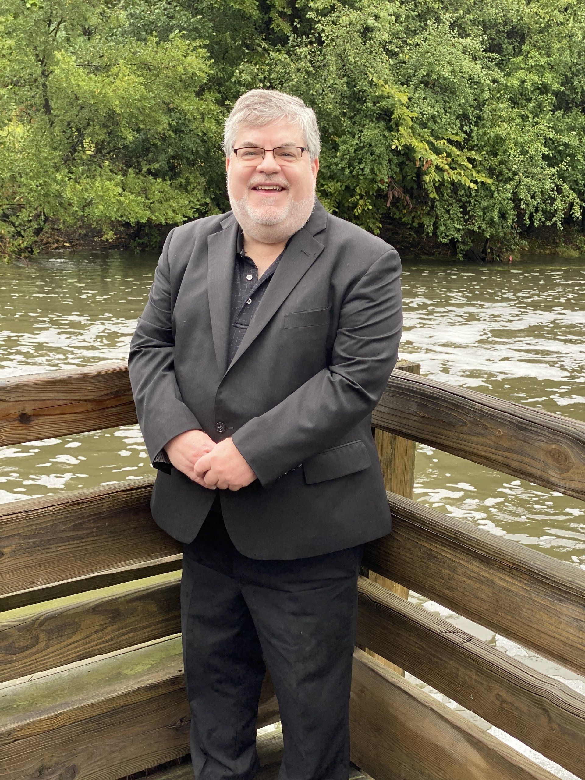 A man in a suit is standing on a bridge overlooking a body of water.