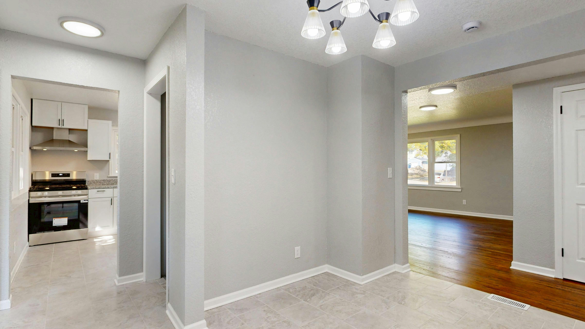 Interior view of a house hallway with a dining room and kitchen visible. Gray walls, white trim, and a chandelier.