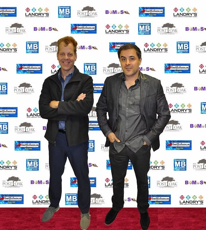 Two men pose together in front of a red carpet step-and-repeat backdrop featuring various company logos.