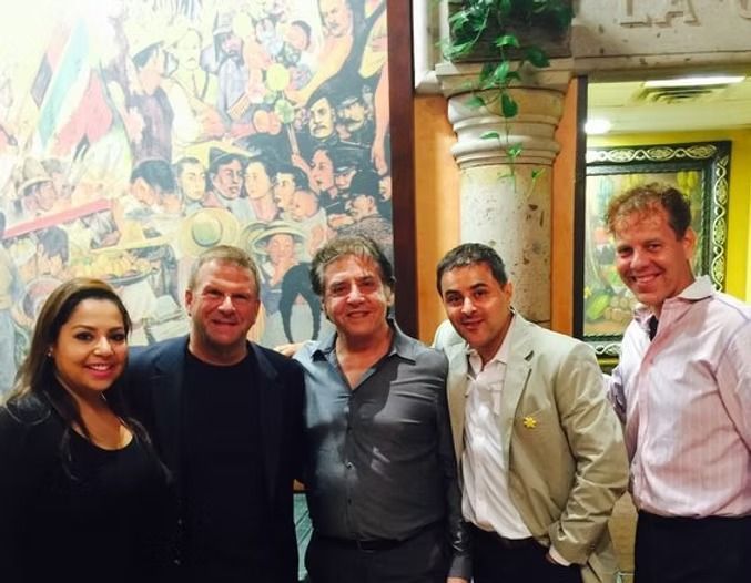 Five people pose for a photo in front of a colorful mural in an indoor setting.