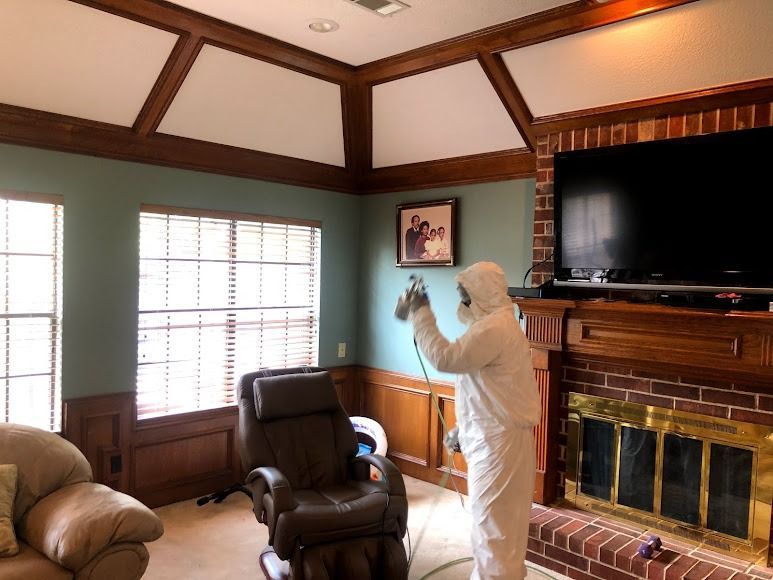 Person in protective suit spraying paint inside room with wood trim.