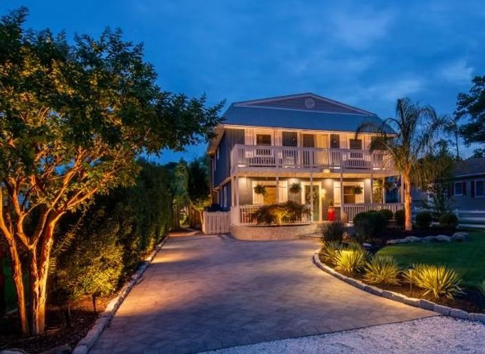 Two-story house with exterior lights illuminating the driveway and landscaping at dusk.