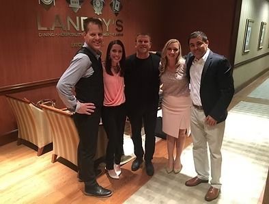 Five people standing in a line smiling for a photo in front of a wood-paneled wall with the Landry’s logo.