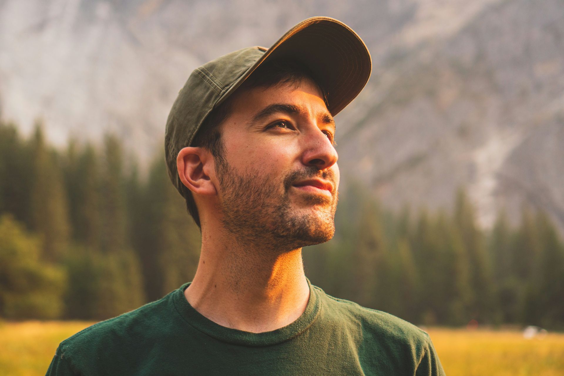 A man wearing a hat and a green shirt is standing in a field.