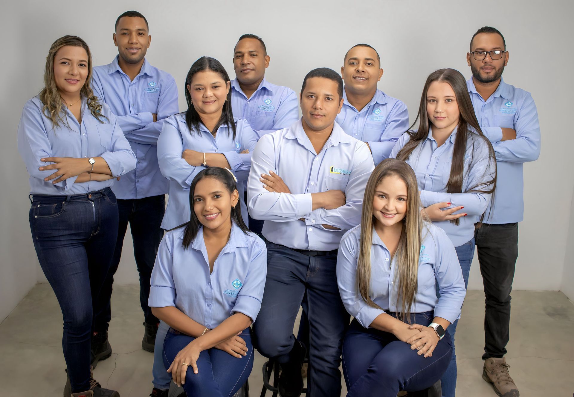 Grupo de 10 personas vestidas con camisetas azules y vaqueros, posando para una foto de equipo en un estudio.