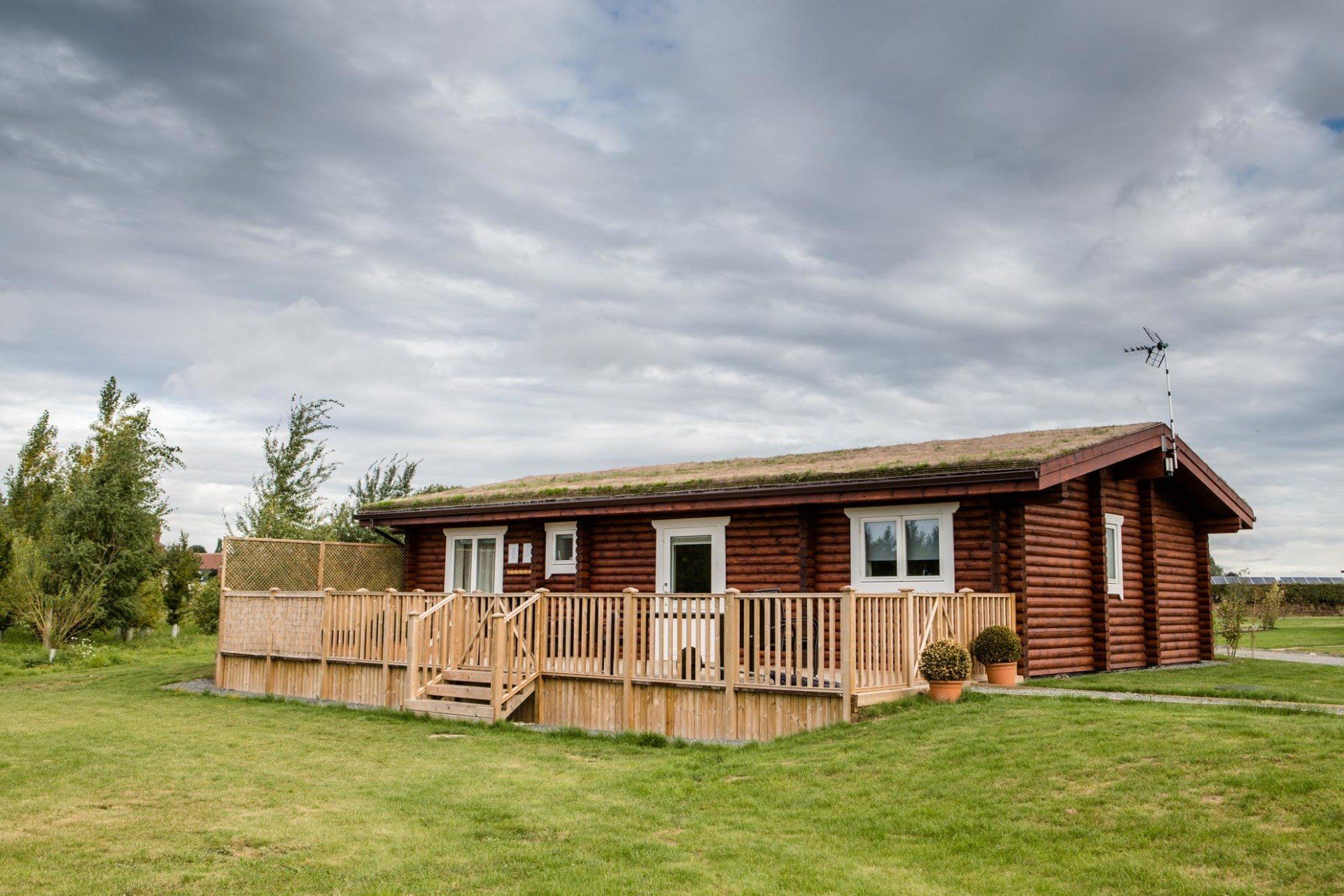 A log cabin with a green roof and a deck is sitting in the middle of a grassy field.