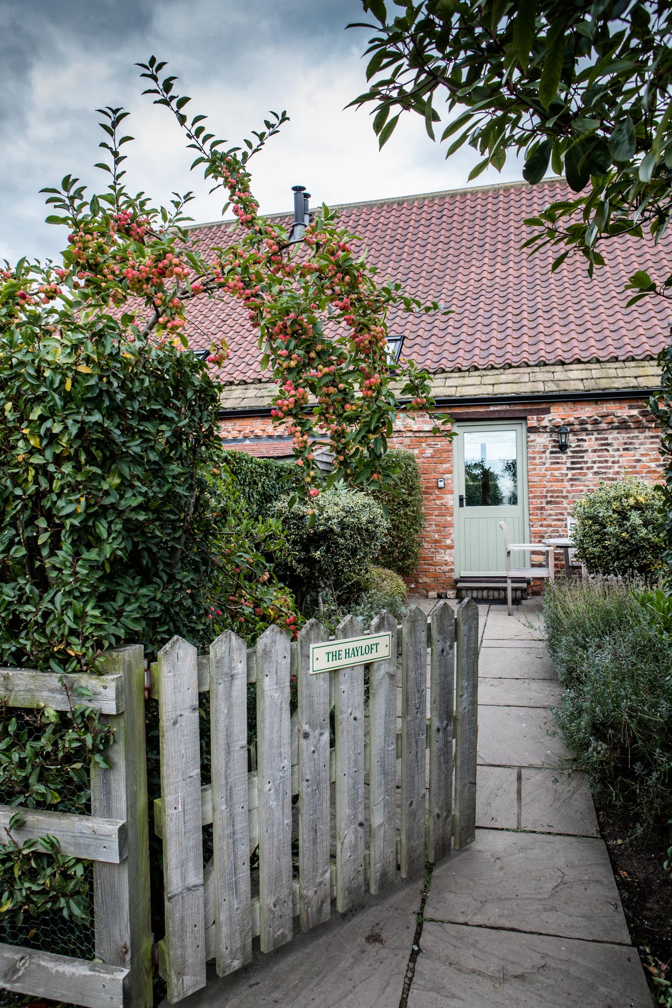 A wooden fence leads to a brick house with a green door.