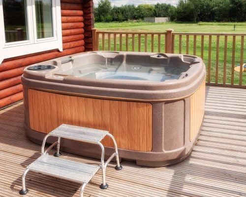 A hot tub is sitting on a wooden deck next to a log cabin.