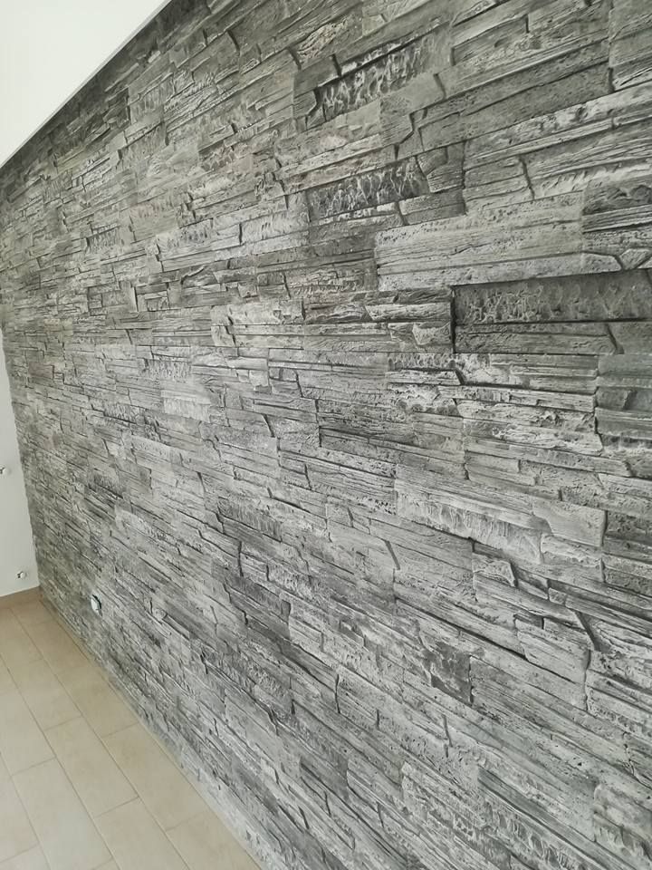 Una parete interna rivestita con pannelli impiallacciati effetto pietra grigia, accanto a un pavimento in legno chiaro.