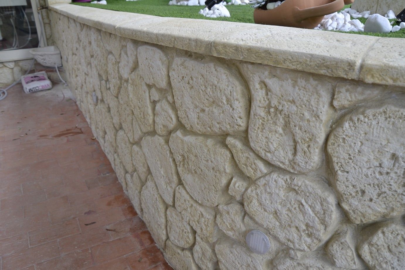 Un muro curvo e basso, realizzato in pietre rustiche di colore chiaro, con un rivestimento in pietra liscio e piatto.