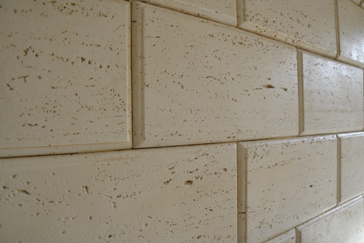 Primo piano di una parete realizzata con piastrelle rettangolari in travertino beige dalla consistenza naturale e porosa.