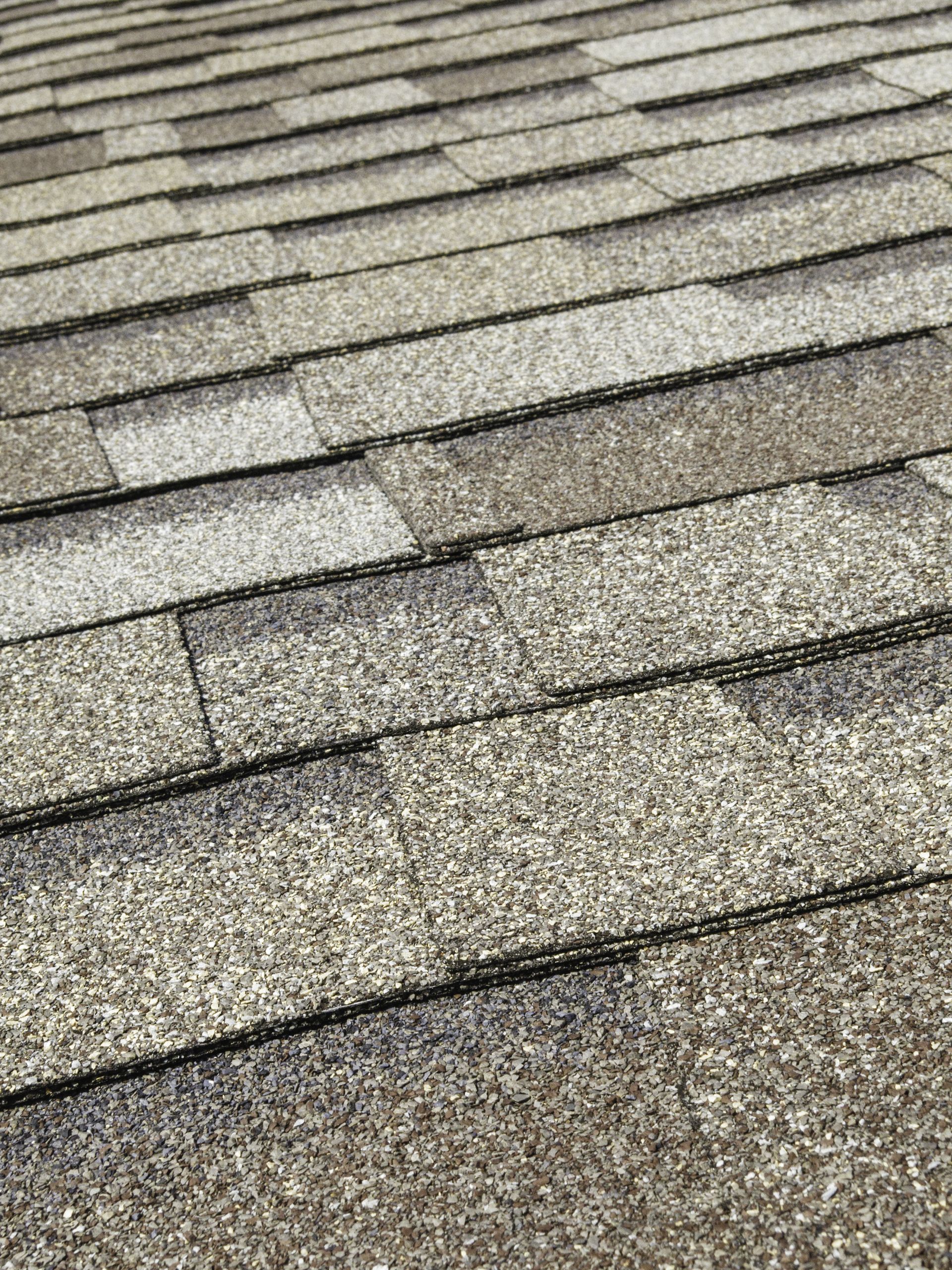 A close-up, angled view of textured, multi-tonal gray architectural asphalt roof shingles.