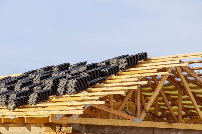 A partially tiled wooden roof frame under construction against a clear blue sky.