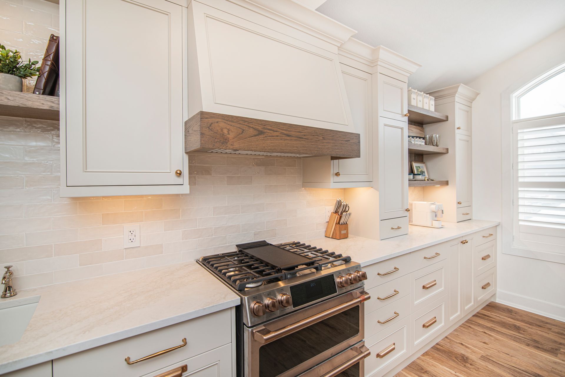 A kitchen with white cabinets , a stove , and a window.