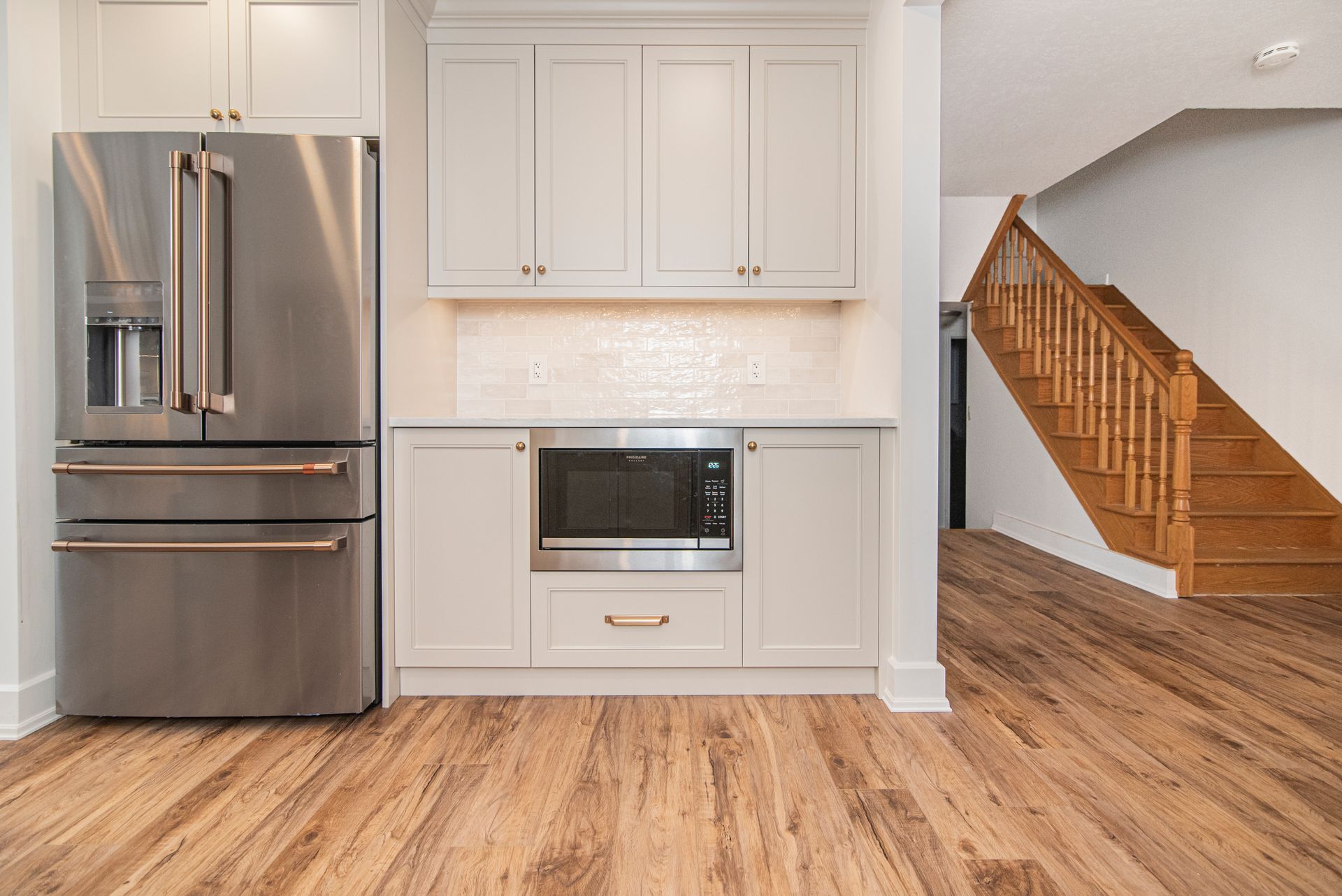 A kitchen with a refrigerator , microwave , and stairs.
