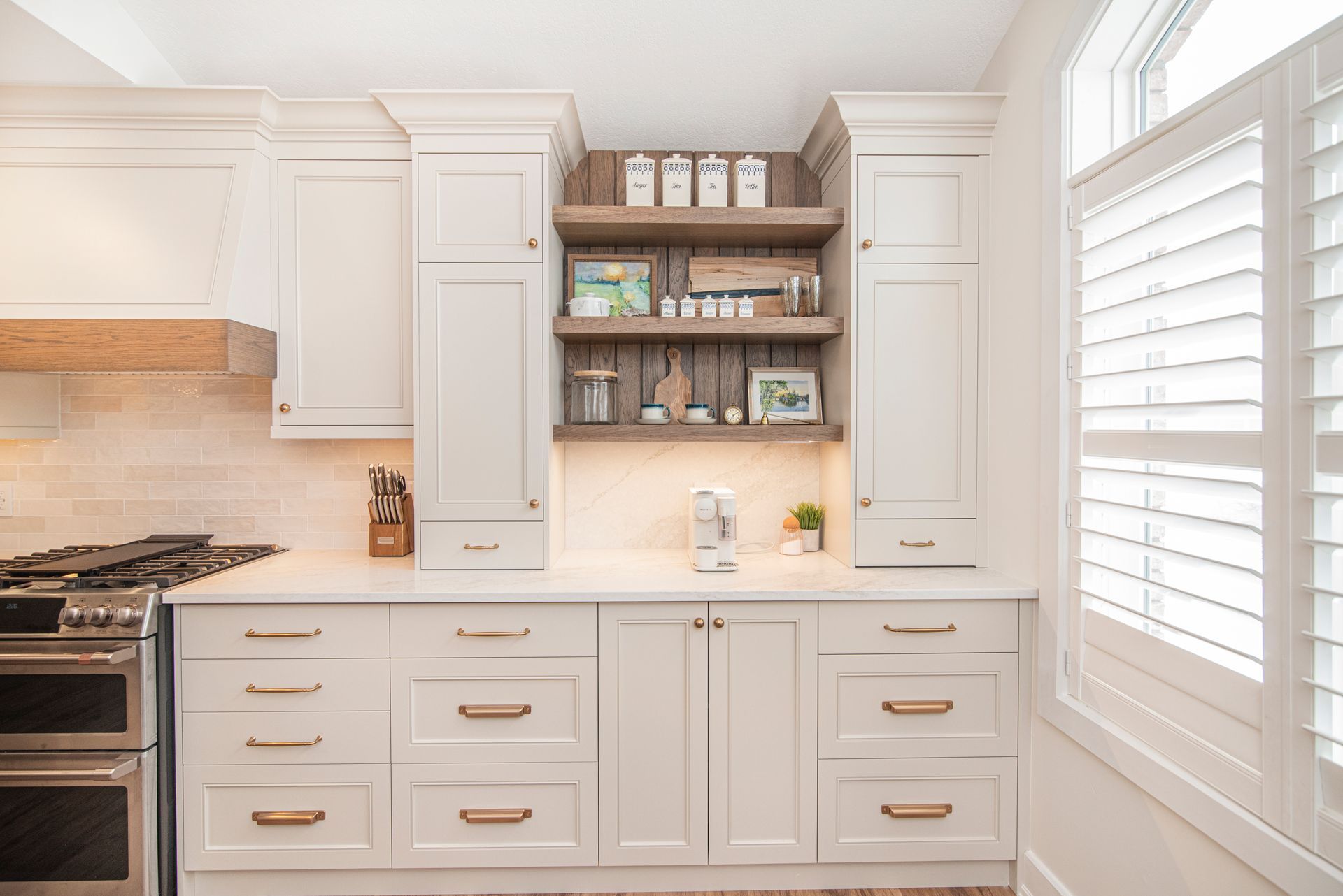 A kitchen with white cabinets , a stove , and a window.