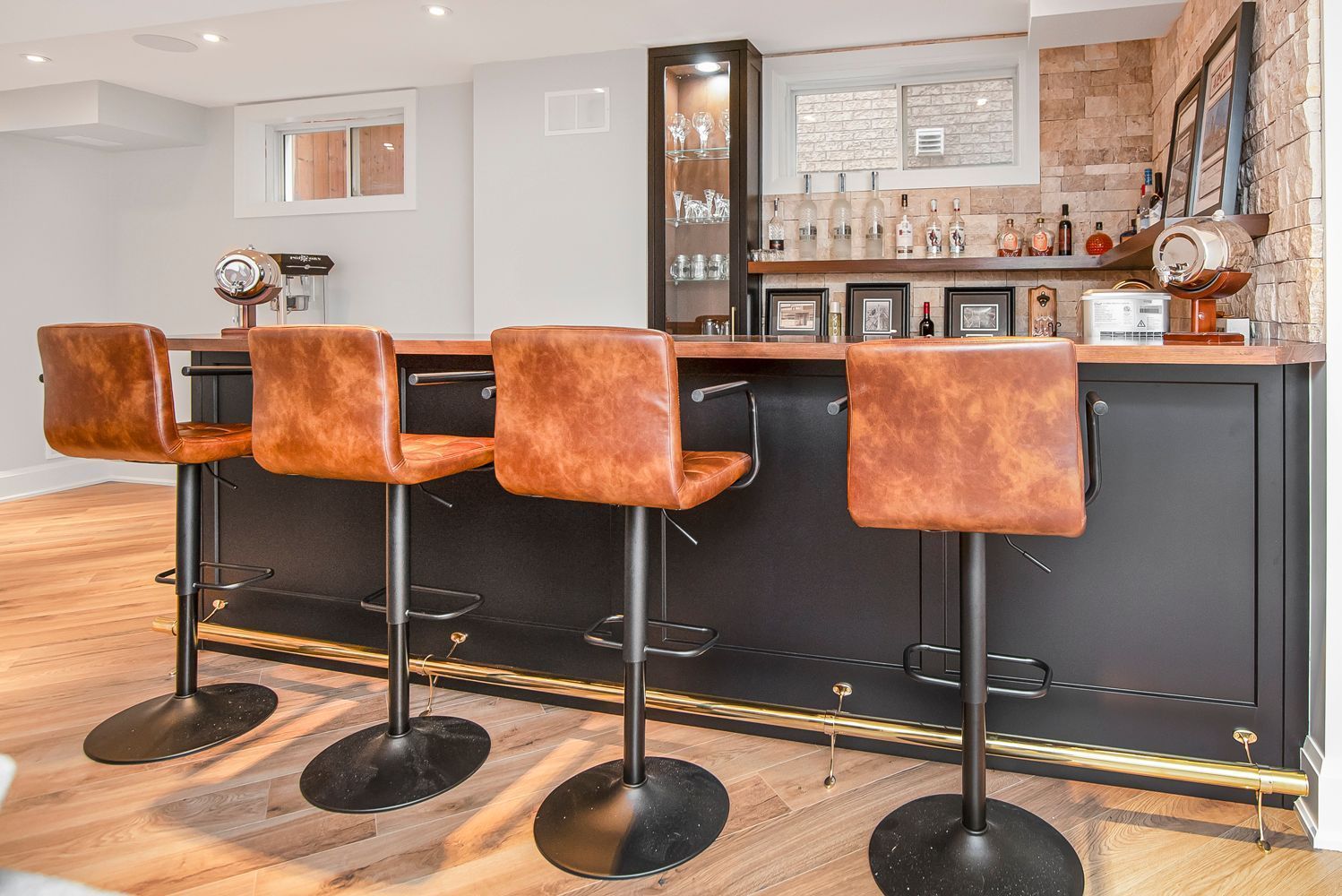 A bar with three brown leather bar stools in a basement.