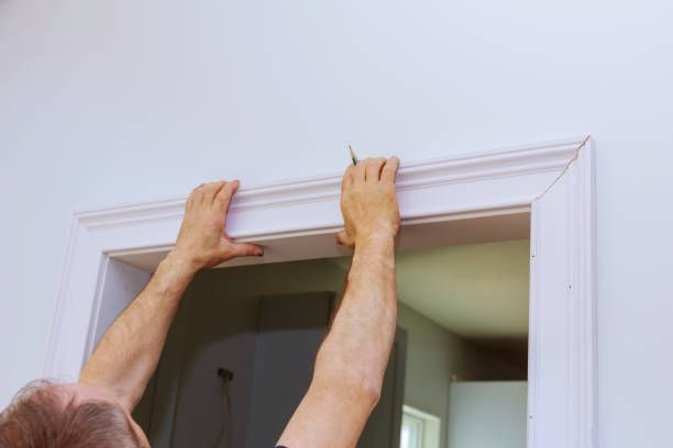 A man is installing molding on a door frame.