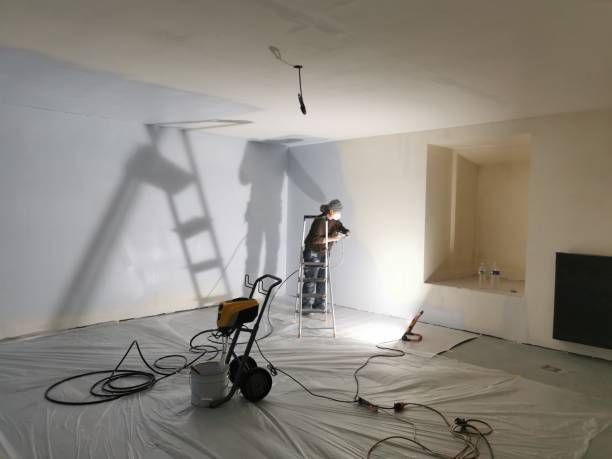 A man on a ladder is painting a wall in a room