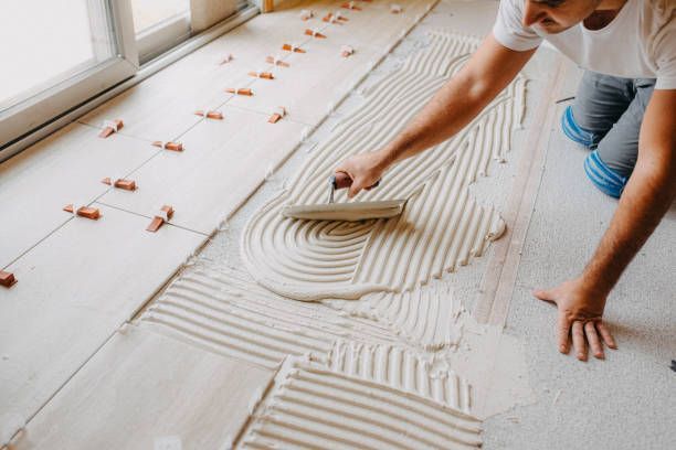 A woman is applying tile adhesive to a tiled floor.