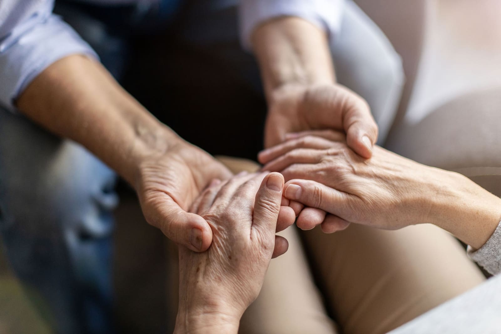 Hands clasped together in a supportive, comforting gesture on a couch.
