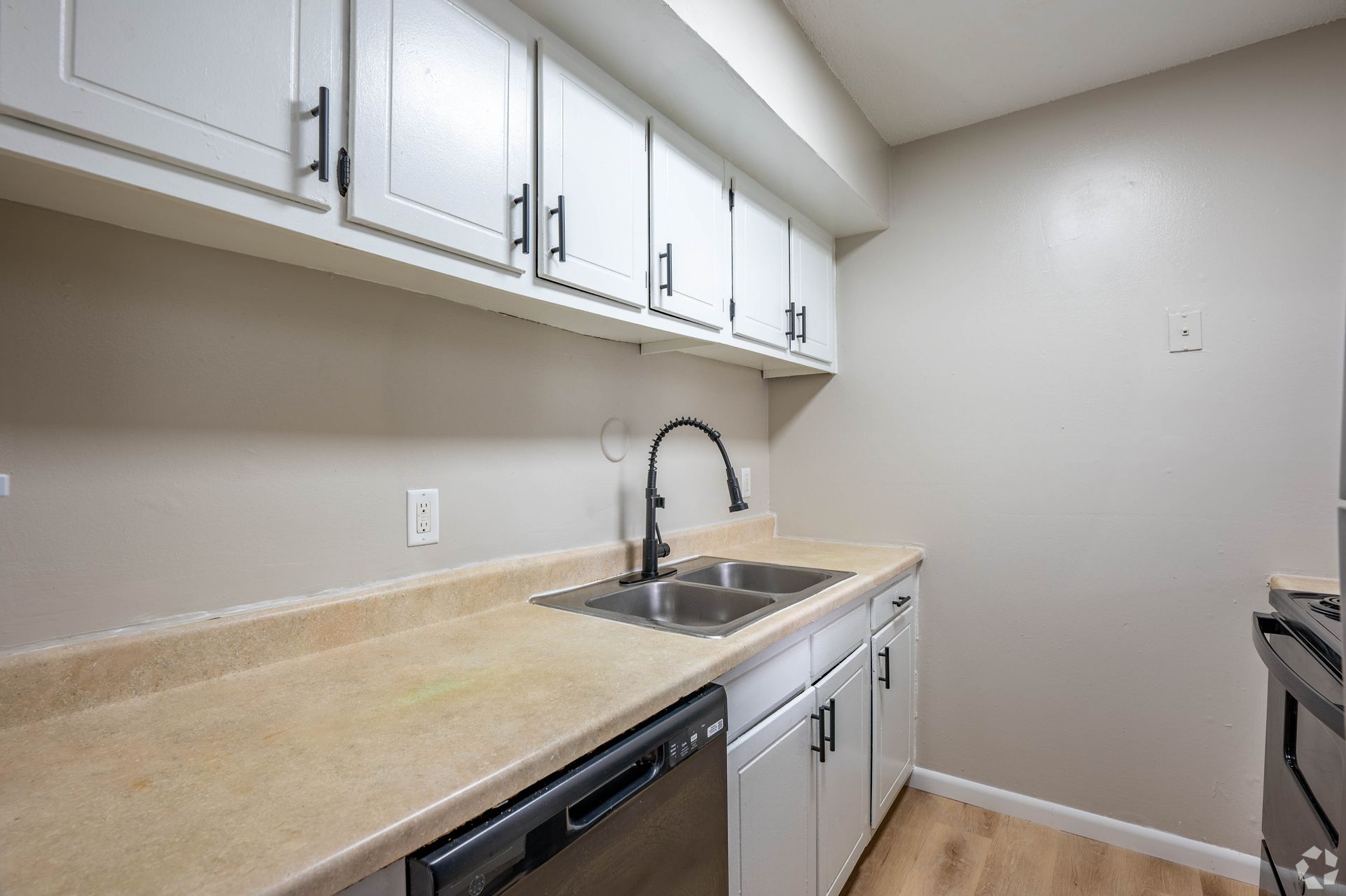Kitchen with white cabinets, tan countertops, and a black faucet and dishwasher.