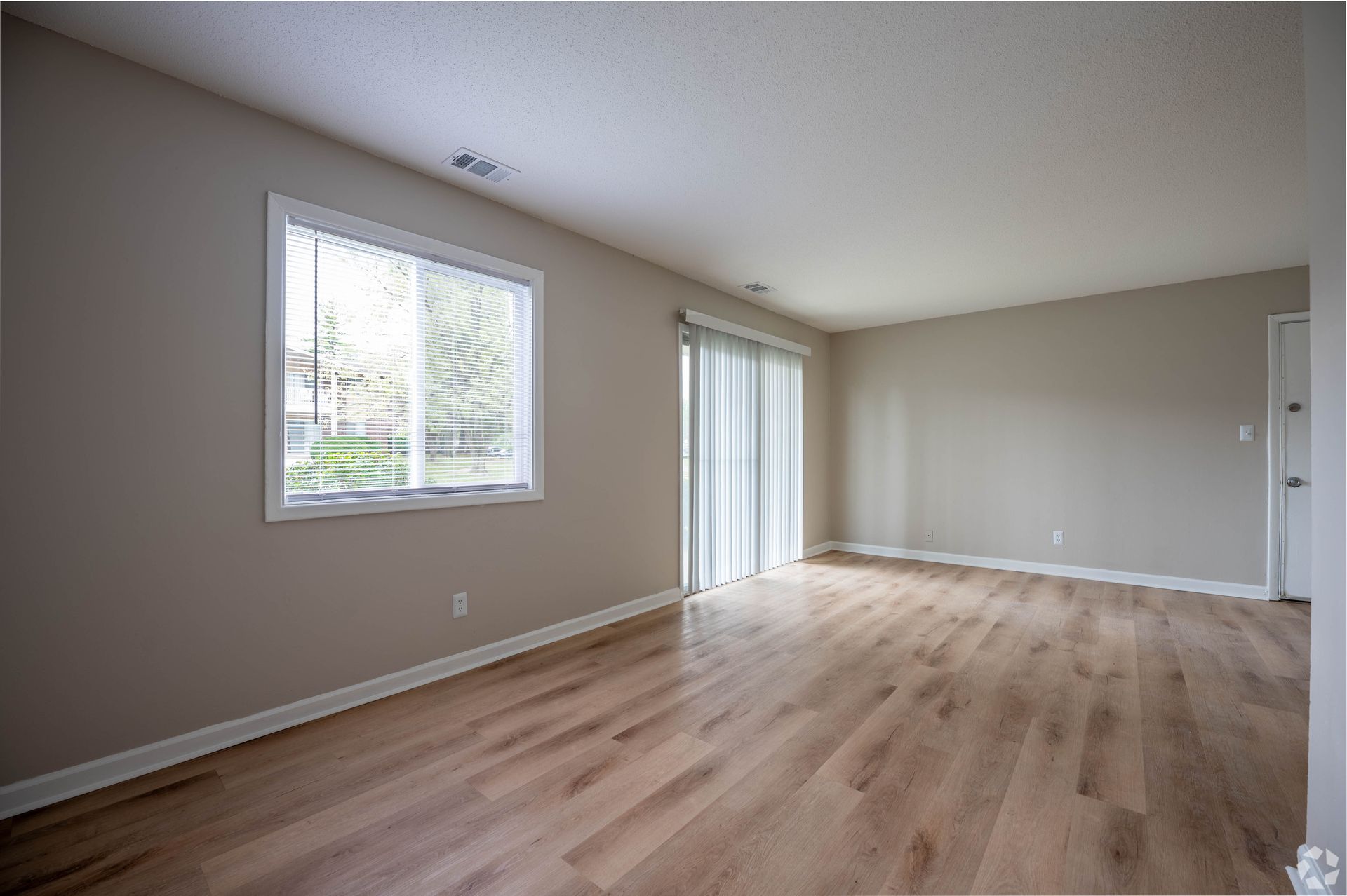 Empty room with wood floors, sliding glass door, window, and beige walls.