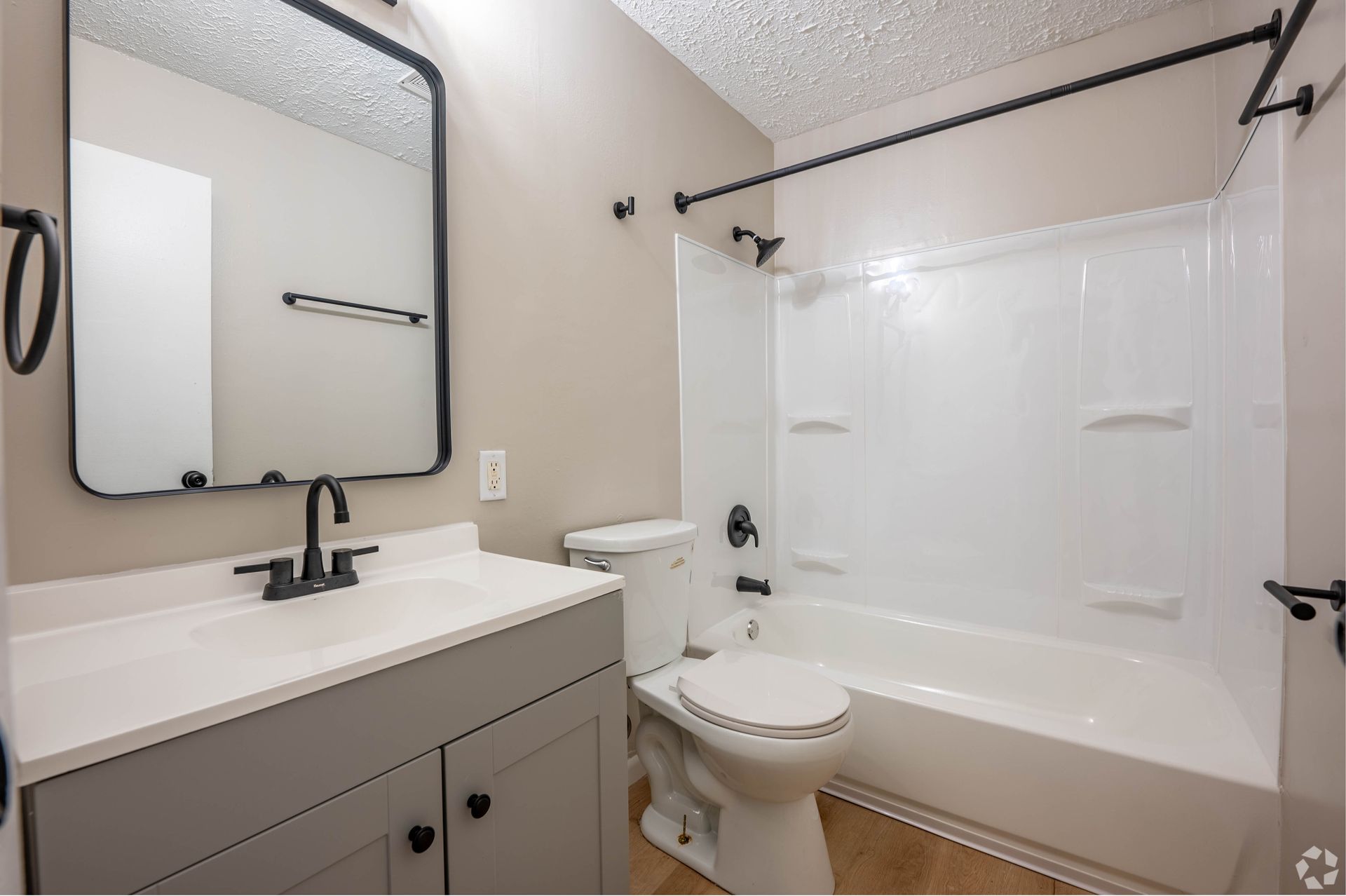 Bathroom with white tub, gray vanity, black fixtures, and a large mirror.