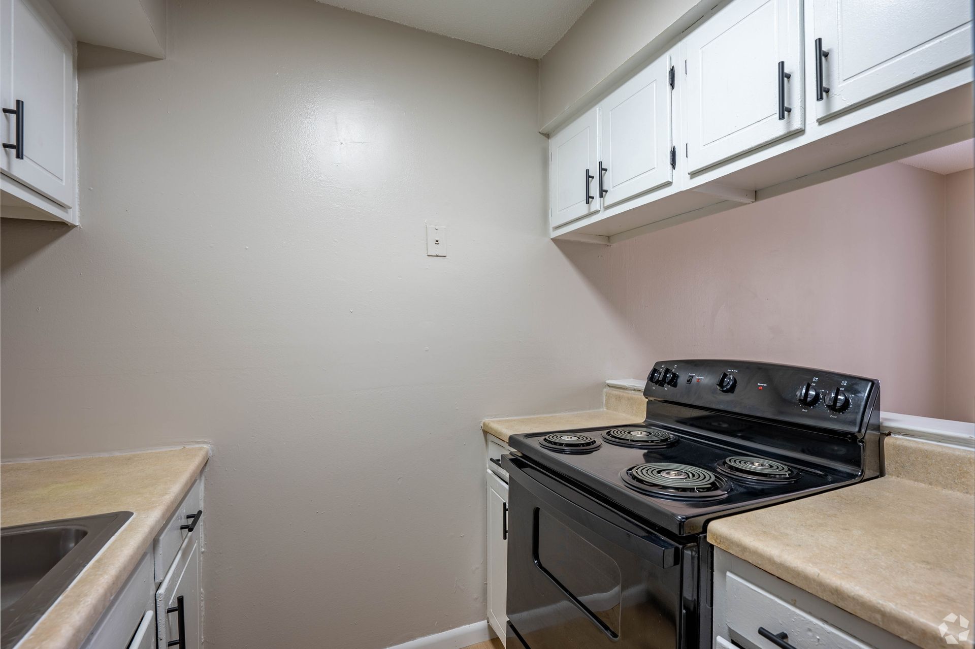 Kitchen with white cabinets, black stove, and tan countertops.