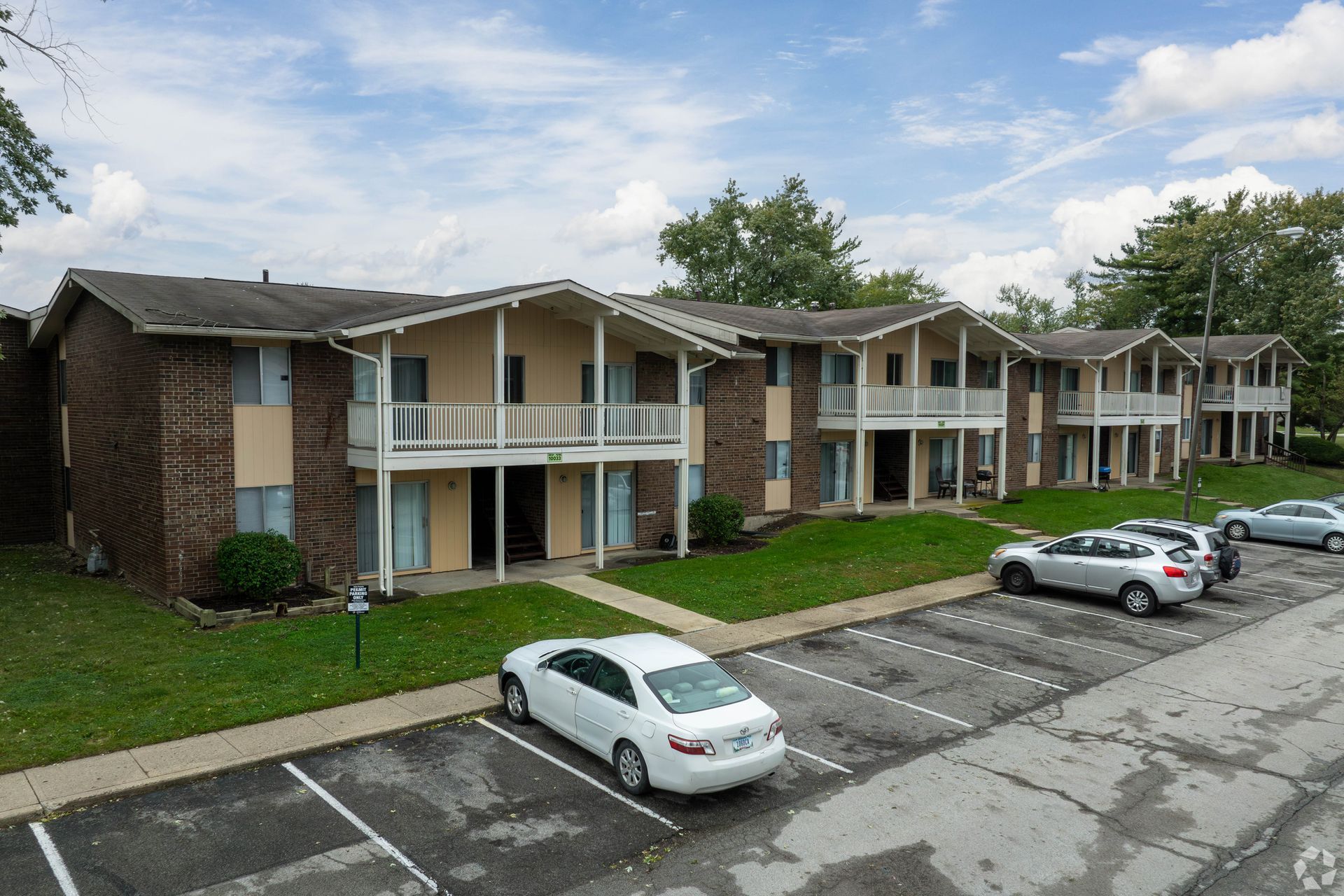 Apartment complex with beige and brown buildings and a parking lot with cars on a sunny day.