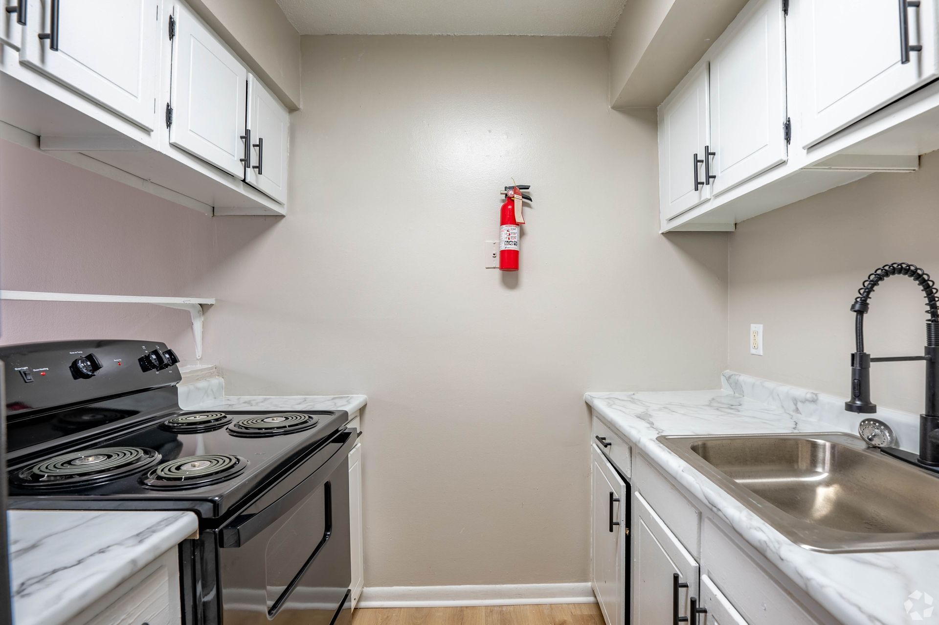 Kitchen with white cabinets, black stove, sink, and a red fire extinguisher on the wall.