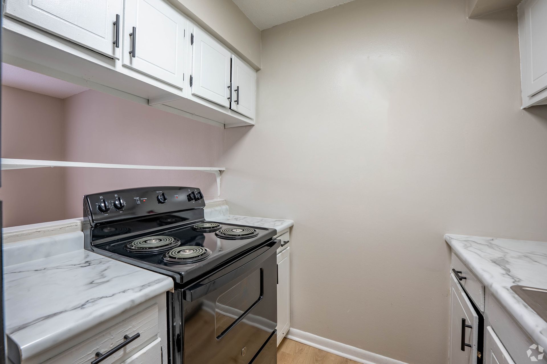 Kitchen with white cabinets, marble countertops, black stove. Beige walls, light wood floor.
