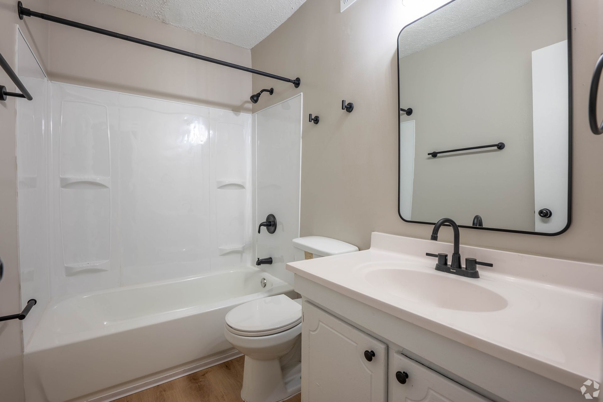 Bathroom with white tub, toilet, sink, and black fixtures.