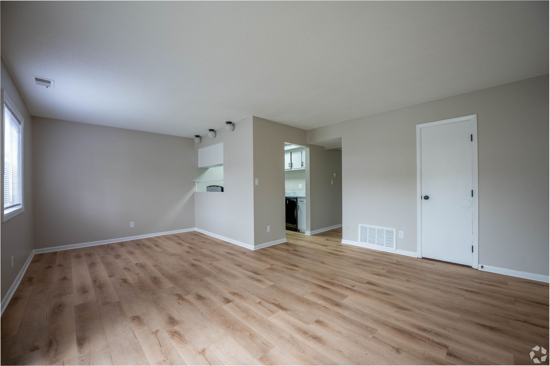 Empty living room with light wood floors and neutral walls. Door and window present.