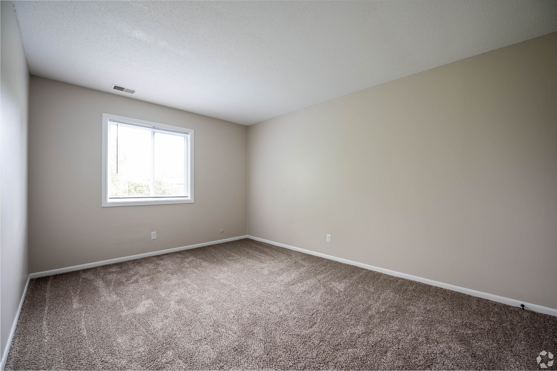 Empty room with tan walls, a window, and brown carpet.
