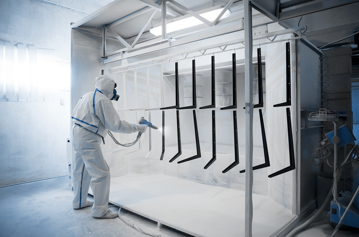 A man in a protective suit is spray painting a metal structure.