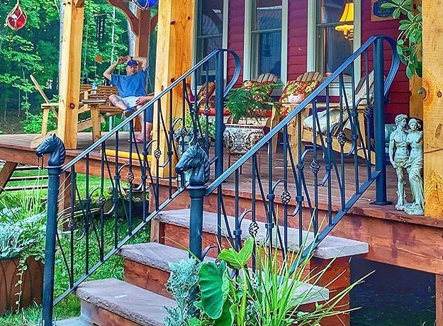 A man is sitting on the porch of a house with a wrought iron railing.