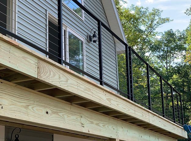 A wooden deck with a black railing is being built on the side of a house.