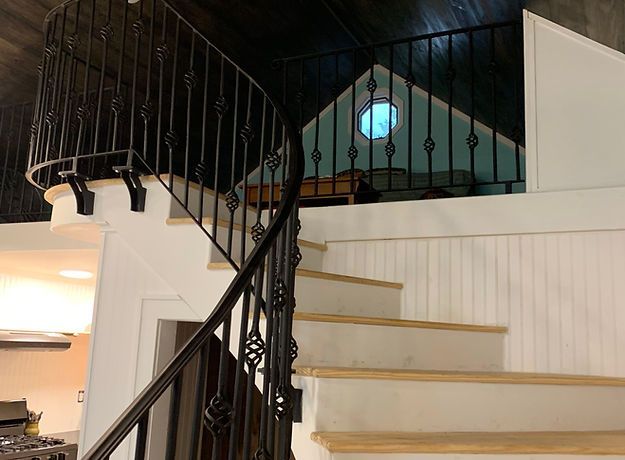 A staircase leading up to a loft with a wrought iron railing.